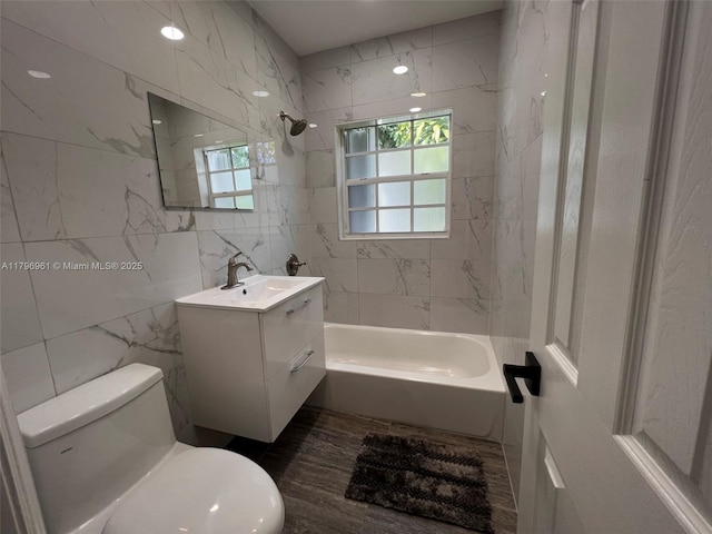 full bath with toilet, tile walls, a wealth of natural light, vanity, and shower / bathtub combination