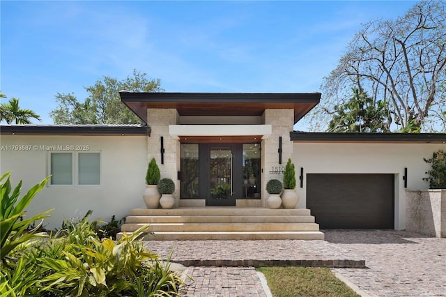 doorway to property with stucco siding, a garage, and decorative driveway