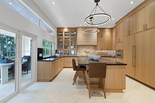 kitchen featuring glass insert cabinets, dark countertops, backsplash, a kitchen island, and stainless steel oven