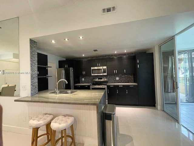kitchen with a sink, tasteful backsplash, visible vents, dark cabinets, and appliances with stainless steel finishes