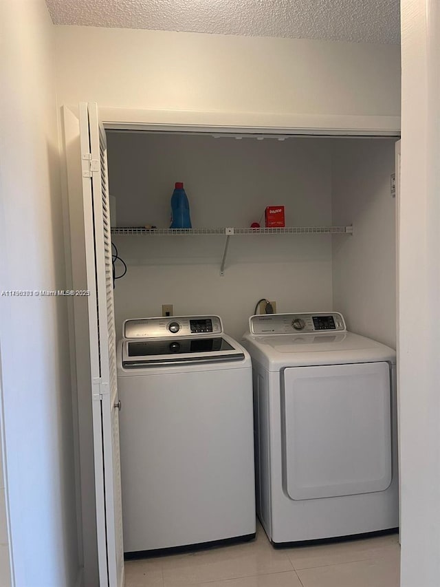 laundry area featuring laundry area, washer and clothes dryer, light tile patterned flooring, and a textured ceiling