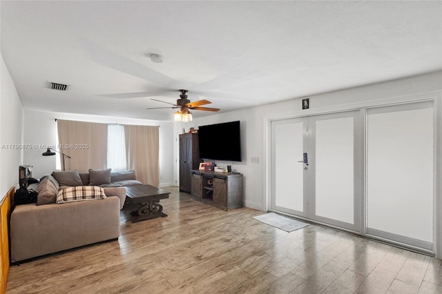 living room featuring ceiling fan, baseboards, visible vents, and light wood-style floors