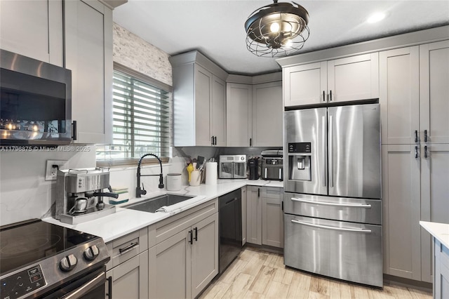 kitchen with gray cabinetry, a sink, light wood-style floors, light countertops, and appliances with stainless steel finishes