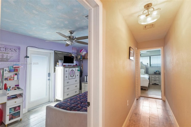 corridor featuring wood-type flooring, baseboards, and visible vents