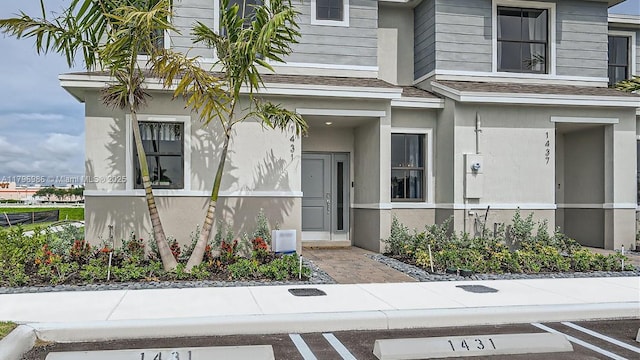 doorway to property with stucco siding, roof with shingles, and uncovered parking