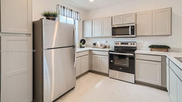 kitchen with gray cabinets, light countertops, light tile patterned floors, and appliances with stainless steel finishes