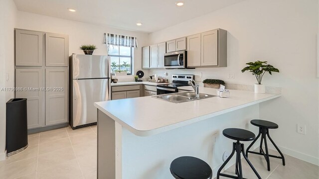 kitchen with a peninsula, a breakfast bar area, a sink, stainless steel appliances, and gray cabinetry
