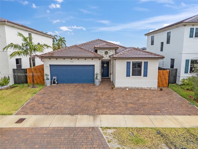view of front facade with fence, an attached garage, stucco siding, a tile roof, and a gate