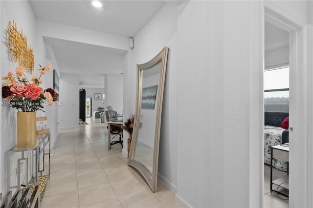 corridor featuring baseboards, a wealth of natural light, and light tile patterned flooring