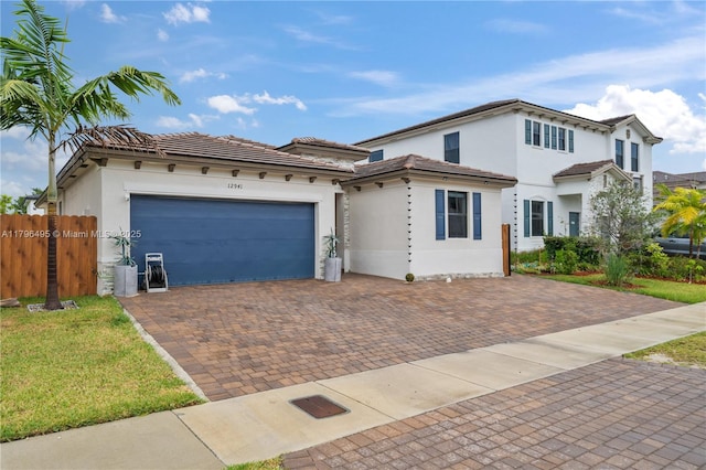 view of front of home with an attached garage, a tiled roof, stucco siding, fence, and decorative driveway