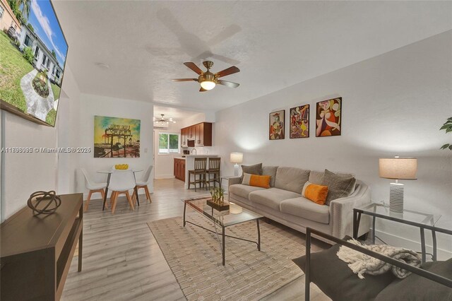 living area featuring light wood-style floors, baseboards, ceiling fan with notable chandelier, and a textured ceiling