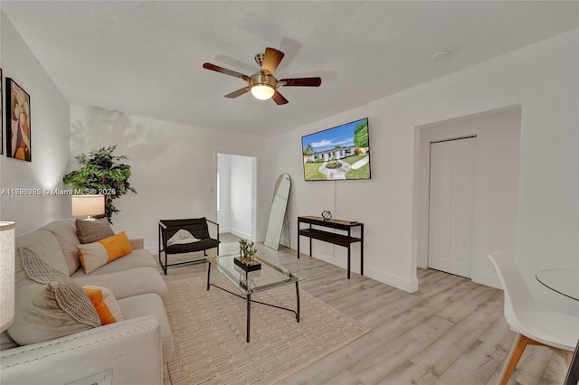 living room with a ceiling fan, baseboards, and light wood-type flooring