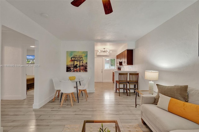 living area with baseboards, light wood finished floors, and ceiling fan with notable chandelier