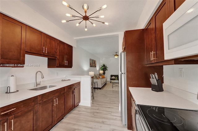 kitchen featuring a sink, freestanding refrigerator, electric range, white microwave, and light wood-style floors