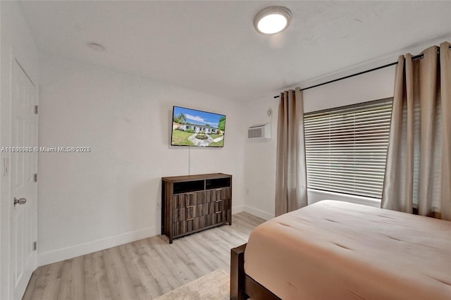 bedroom featuring baseboards, light wood-style flooring, and a wall unit AC