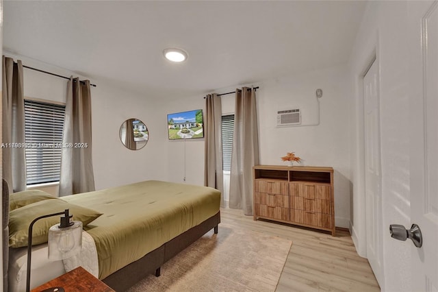 bedroom with multiple windows, light wood-type flooring, baseboards, and a wall mounted AC