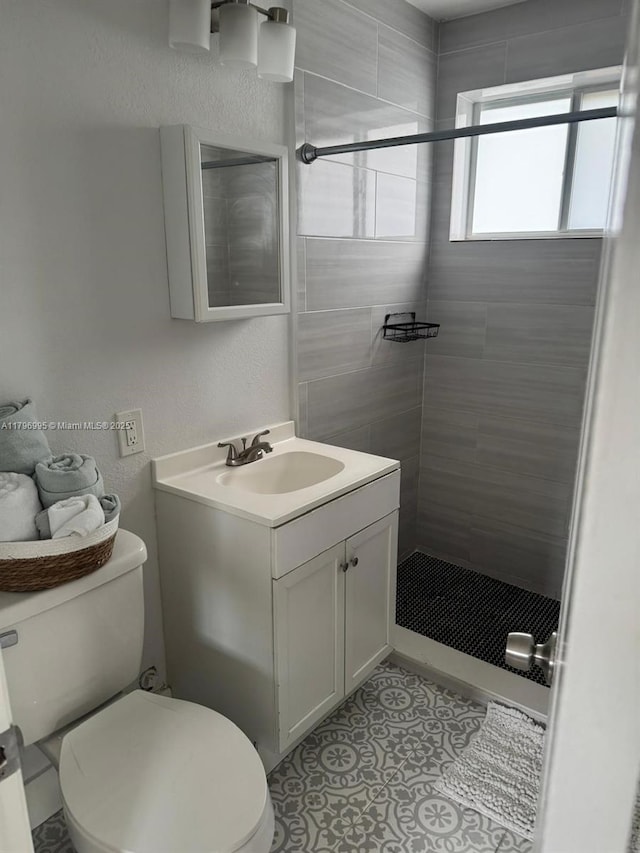 bathroom featuring tile patterned floors, vanity, toilet, and a tile shower