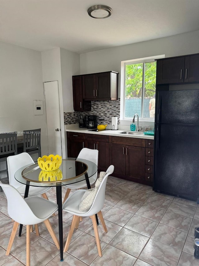 kitchen featuring a sink, tasteful backsplash, freestanding refrigerator, light countertops, and dark brown cabinets