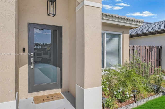 property entrance featuring stucco siding, a tiled roof, and fence