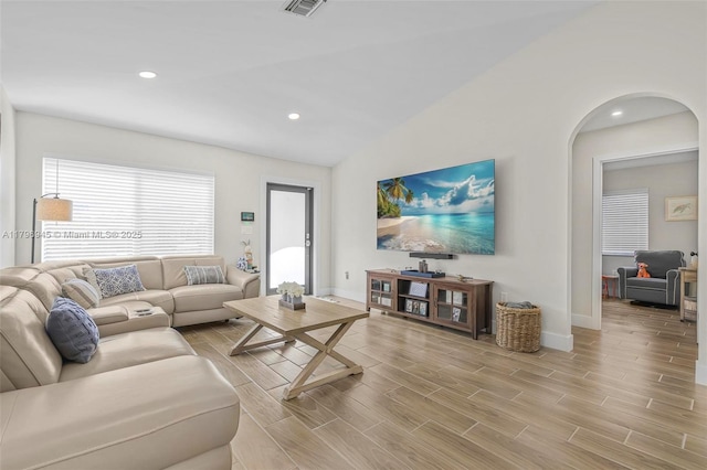 living room with light wood-style flooring, baseboards, arched walkways, and recessed lighting
