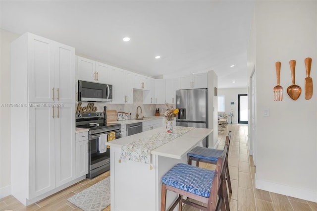 kitchen with a breakfast bar area, a center island, a sink, light countertops, and appliances with stainless steel finishes