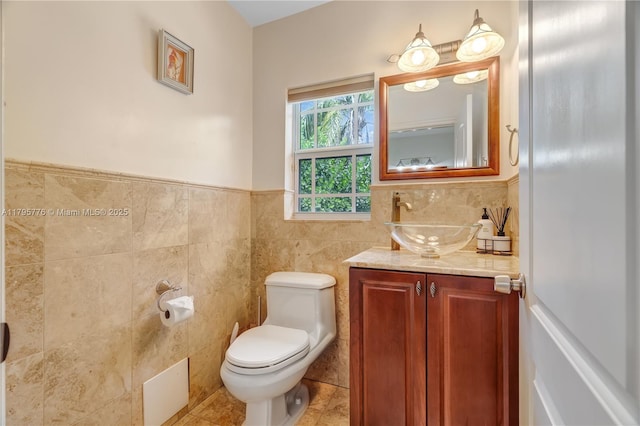 bathroom with tile walls, toilet, tile patterned flooring, vanity, and a wainscoted wall