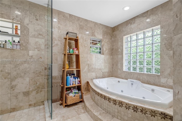full bathroom with tile walls, a tub with jets, and plenty of natural light