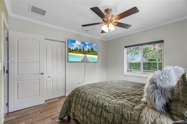 bedroom with a closet, visible vents, wood finished floors, and ornamental molding