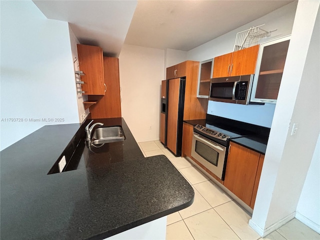 kitchen with glass insert cabinets, brown cabinets, a sink, dark countertops, and stainless steel appliances