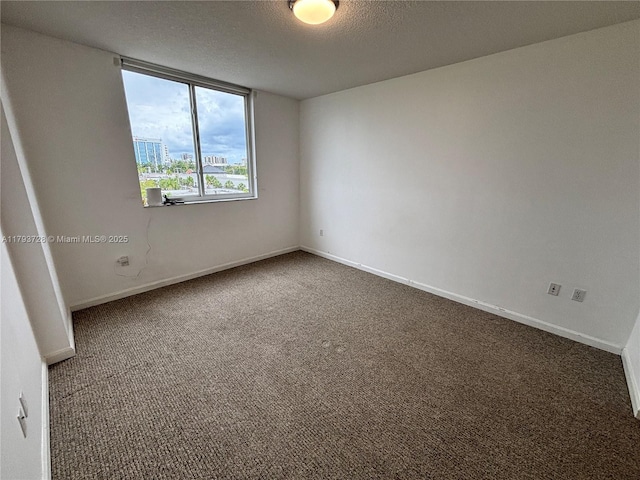 carpeted spare room with a textured ceiling and baseboards