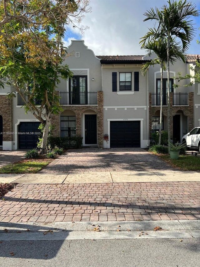 view of front of house with a balcony, a tiled roof, decorative driveway, an attached garage, and stucco siding