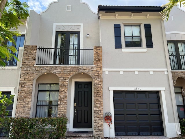 view of front facade with a balcony, stone siding, stucco siding, and a garage