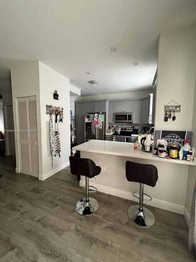 kitchen featuring a peninsula, a breakfast bar area, stainless steel appliances, dark wood-type flooring, and gray cabinetry