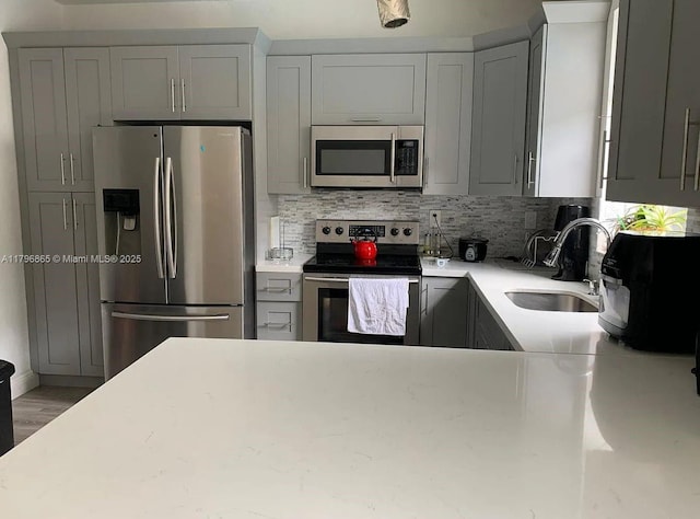 kitchen featuring wood finished floors, a sink, gray cabinetry, appliances with stainless steel finishes, and decorative backsplash