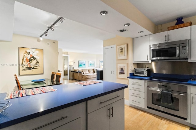 kitchen with light wood-style flooring, dark countertops, track lighting, visible vents, and appliances with stainless steel finishes