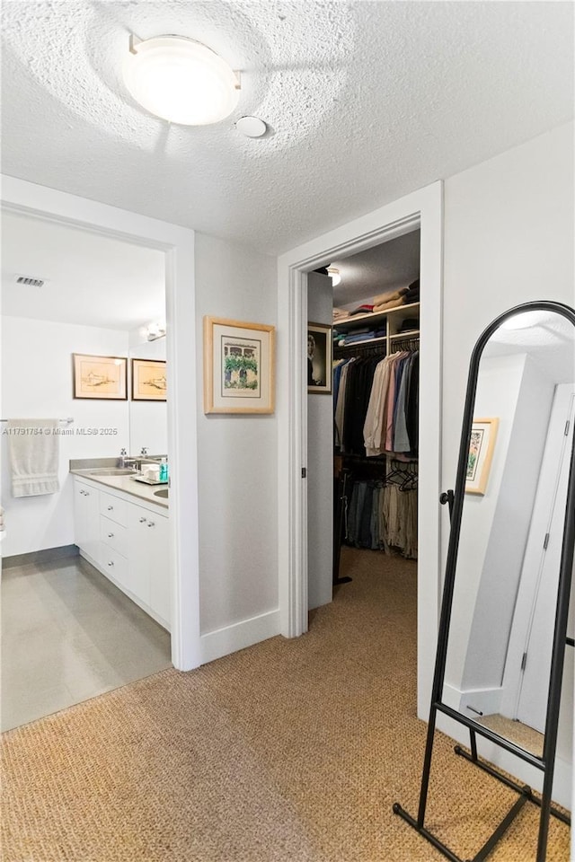hall with baseboards, a textured ceiling, visible vents, and a sink