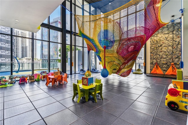 game room featuring floor to ceiling windows, a view of city, and a towering ceiling