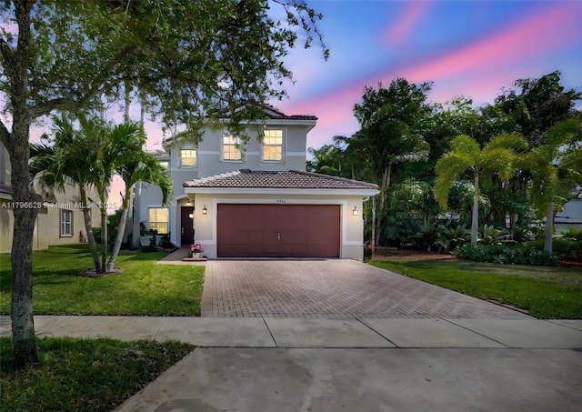 mediterranean / spanish house with a garage, a tiled roof, stucco siding, a lawn, and decorative driveway