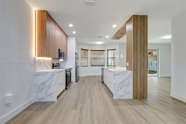 kitchen with a sink, stainless steel appliances, visible vents, light wood finished floors, and modern cabinets