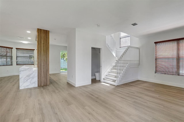 unfurnished living room with light wood-style flooring, stairs, baseboards, and visible vents