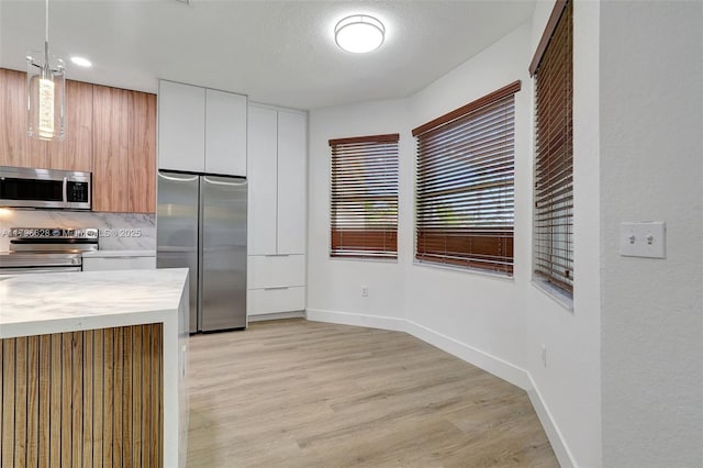 kitchen featuring stainless steel appliances, light wood-type flooring, modern cabinets, baseboards, and light countertops