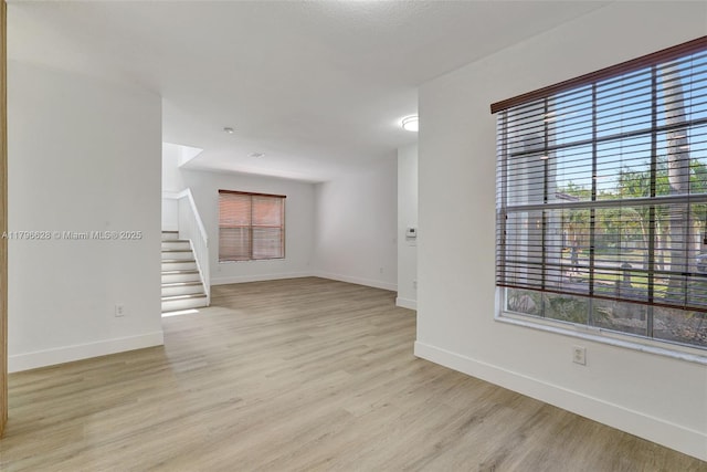 spare room featuring light wood-style flooring, baseboards, and stairs