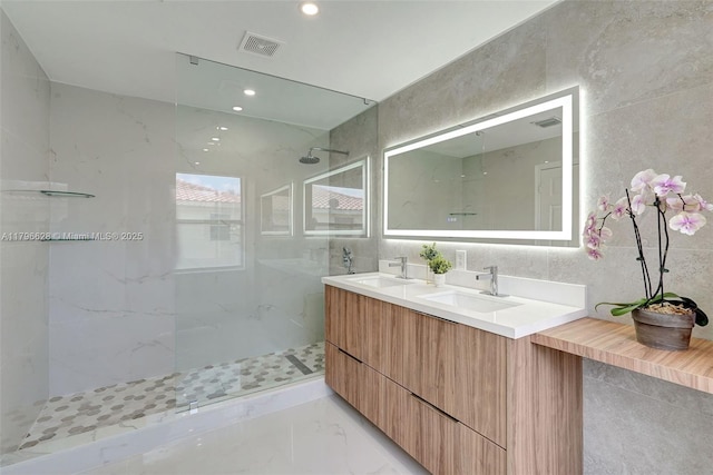 bathroom with a marble finish shower, tile walls, visible vents, and a sink