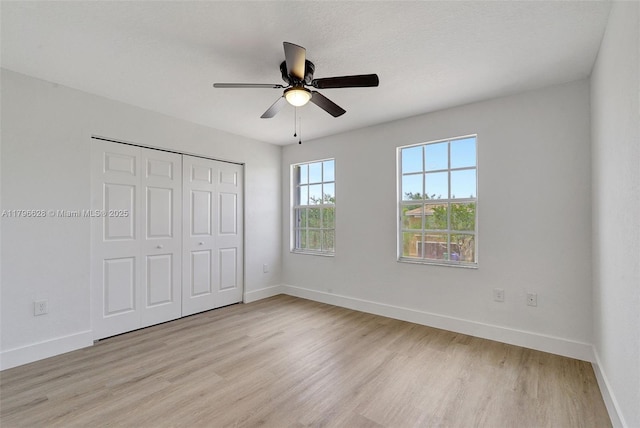 unfurnished bedroom featuring ceiling fan, light wood-style flooring, a closet, and baseboards