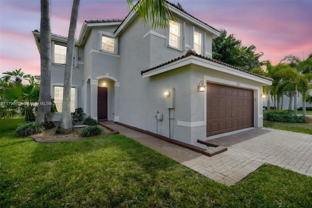mediterranean / spanish home featuring a garage, a tiled roof, stucco siding, a front lawn, and decorative driveway