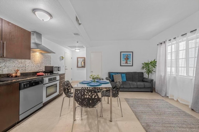 1300 Pennsylvania Ave Unit 104, Miami Beach, FL 33139 - kitchen featuring dark brown cabinets, wall chimney exhaust hood, dark countertops, tasteful backsplash, and appliances with stainless steel finishes