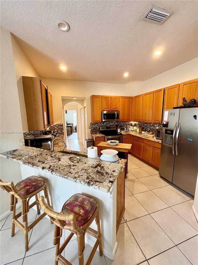 16724 NW 8th St, Pembroke Pines, FL 33028 - kitchen featuring a peninsula, brown cabinets, visible vents, arched walkways, and appliances with stainless steel finishes