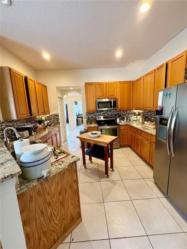 16724 NW 8th St, Pembroke Pines, FL 33028 - kitchen featuring arched walkways, stainless steel appliances, brown cabinetry, and decorative backsplash