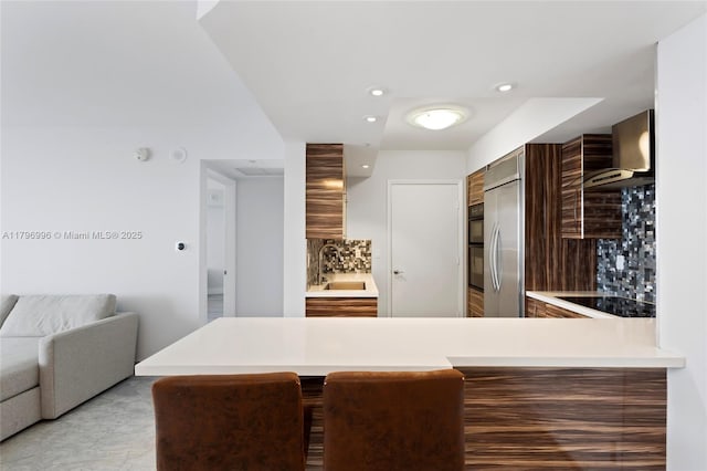 kitchen with wall chimney exhaust hood, black electric stovetop, a sink, tasteful backsplash, and modern cabinets
