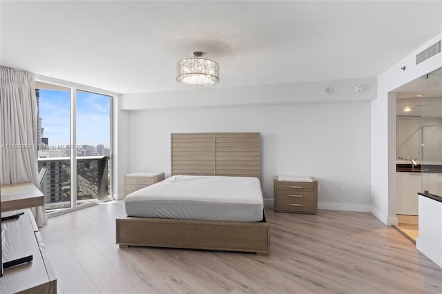 bedroom featuring a wall of windows, light wood-style floors, access to outside, baseboards, and a city view
